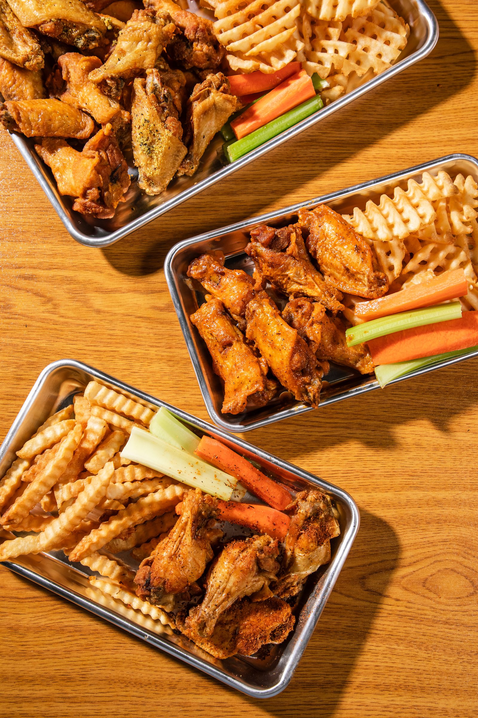 Two trays of wings and waffle fries on a wooden table