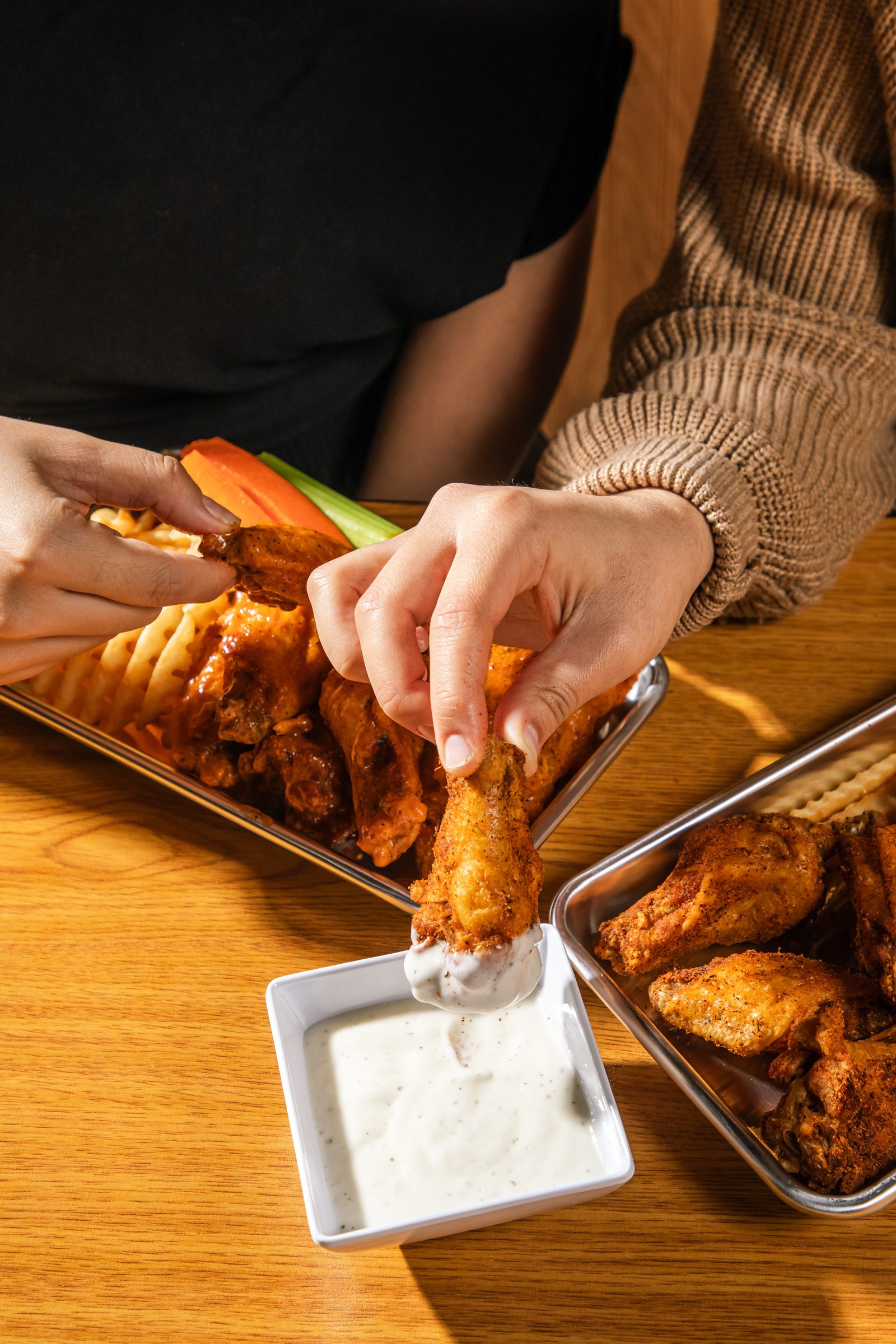 A hand picking up a sauced chicken wing from a tray at Wing It